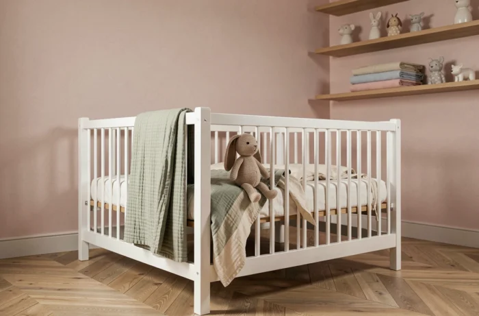 Chambre de bébé décorée avec style dans des tons naturels, avec un lit à barreaux en bois blanc, des linges en coton bio et des étagères en chêne