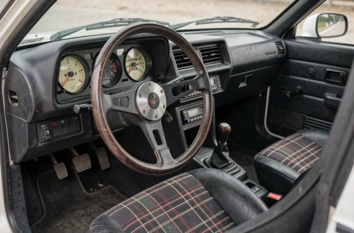 Intérieur vintage de la Peugeot 305 GTI 16 avec volant sport, tableau de bord rétro et sièges à carreaux typiques des années 1980